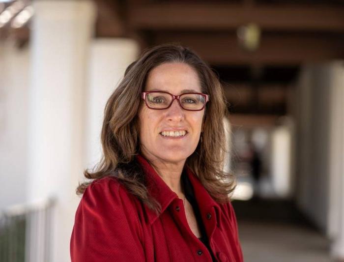 Headshot of Julie Scaff, brown medium length hair wearing a red jacket and red glasses